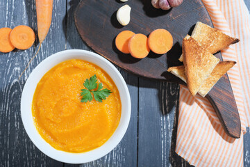 carrot puree spicy soup on rustic table. autumn vegan menu, croutons on cutboard. vitamin fall and...