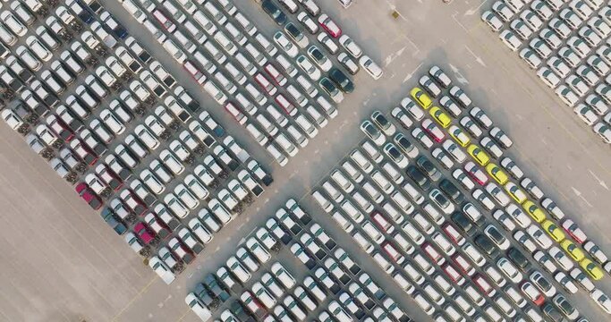 Aerial view of large parking new cars distribution center of modern seaport. Lot of vehicles waiting for sale and transportation shipping by freight cargo vessel ship. Automobile industry.