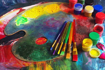 Multi-colored art palette, brushes, tubes of paint lying on the canvas.