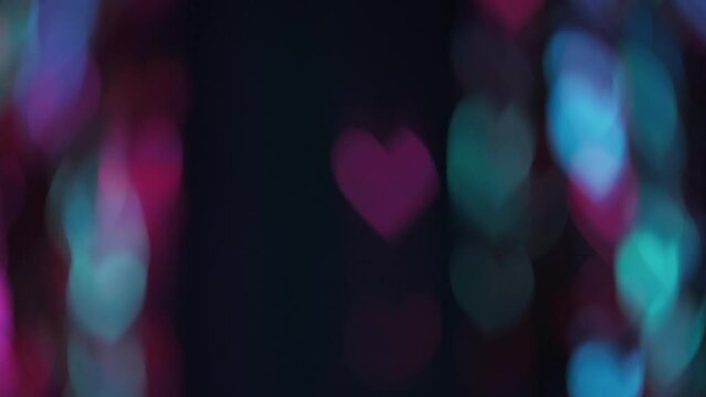 Bokeh light. Romantic overlay. Love symbol. Blur gleam. Defocused fluorescent neon pink blue color hearts glow motion on dark black abstract background.