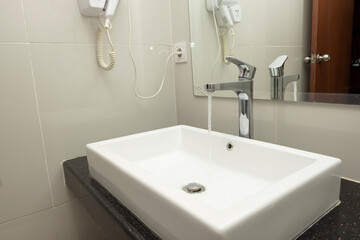 Bathroom sink basin and closed chrome faucet washbasin. Silver taps on ceramic beige tiles wall, square white wash basin. Modern minimal concept.