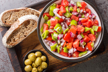 Trampo ensalada salad made with tomatoes, peppers, and onions served with olive and bread closeup on the wooden board on the table. Horizontal top view from above
