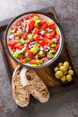 Salad of bell green peppers, tomatoes and onions served with olives and homemade bread close-up on a wooden board on the table. Vertical top view from above