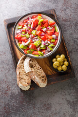 Trampo salad is a traditional Majorcan dish made with tomatoes, peppers, and onions served with olive and bread closeup on the wooden board on the table. Vertical top view from above