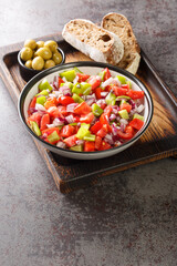 Salad of bell green peppers, tomatoes and onions served with olives and homemade bread close-up on a wooden board on the table. Vertical