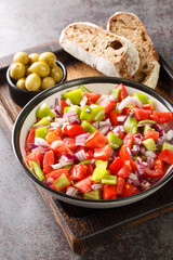 Trampo salad is a traditional Majorcan dish made with tomatoes, peppers, and onions served with olive and bread closeup on the wooden board on the table. Vertical