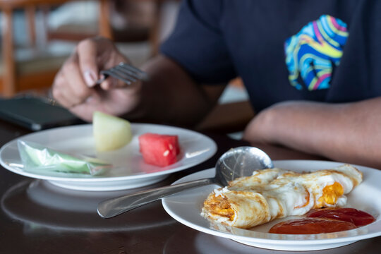 Fried eggs with sauce and spoon on the white dish.
Cropped image of a young casual man eating fresh fruit for breakfast as a bokeh foreground.