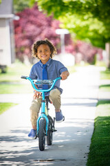 A cute bi-racial boy riding a small bicycle on his way to school dressed in a shirt and tie. Riding...