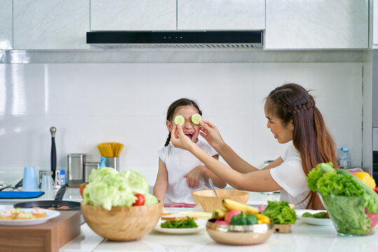 Mother and daughter playing cucumber in cooking time of family