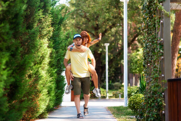 Summer enjoy. Boyfriend piggyback ride his girlfriend at the park. Happy caucasian woman with tattoos and bearded smiling man spend time together. The concept of relationship psychology