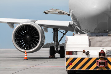 Close-up tow truck near the passenger airplane. Close-up of engine and main landing gear of aircraft
