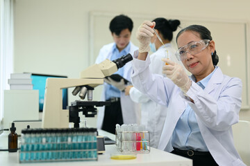 Smiling middle aged scientist working analysis with liquid test tube in the science research laboratory