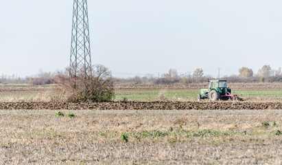 Winter agricultural landscape. Winter plowing arable land with green tractor.