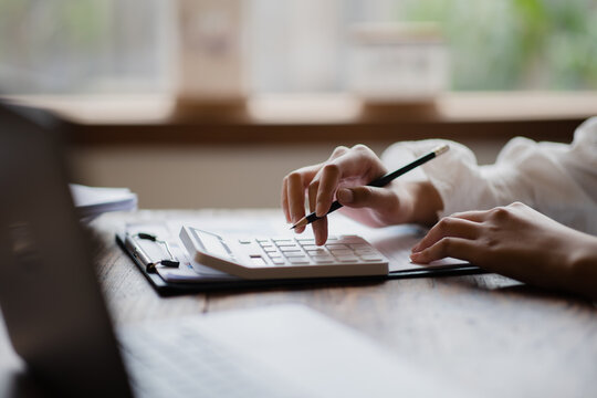 Close Up Of Businesswoman Or Accountant Hand Holding Pen Working On Calculator To Calculate Business Data, Accountancy Document And Laptop Computer At Office, Business Concept.