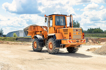 Obraz premium A large front loader transports crushed stone or gravel in a bucket at a construction site or concrete plant. Transportation of bulk materials. Construction equipment. Bulk cargo transportation.