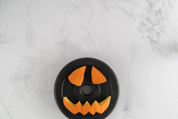 Dumbbell barbell weight plate with Halloween pumpkin pieces cut out. Spooky carved face elements....