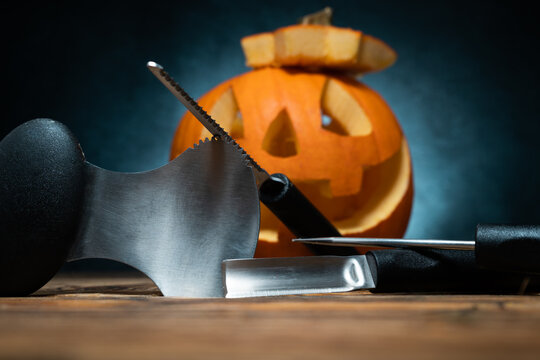 Halloween pumpkin carving tools spoon gutter and saw blades, with carved Jack Lantern (Jack-o'-lantern) spooky laughing, scary head in background. 