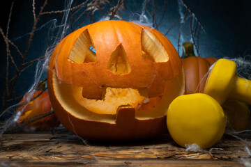 Carved Halloween Jack-o'-lantern spooky pumpkin and yellow dumbbells, covered with spider web....