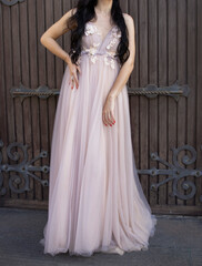 Obraz premium a girl with long dark hair, in a beautiful pink dress, stands on the street, during the day. Wedding fashion, gentle look, runaway bride. Actual dresses