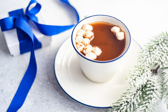 Cup of hot chocolate with miniature marshmallows next to a wrapped gift box and fir branch