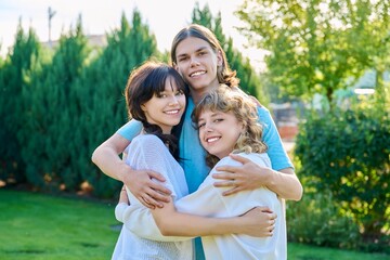 Fototapeta premium Portrait of three happy teenage friends hugging looking at camera