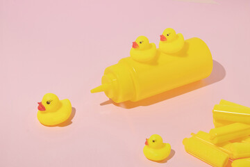 Creative layout made with yellow rubber ducks , mustard bottle and hair rollers on pastel pink background. Surreal concept. Retro style aesthetic toy idea.