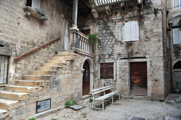 Old peaceful corner of Trogir, Croatia. Old town ruins with bench outside old house with staircase and ornamented railings.