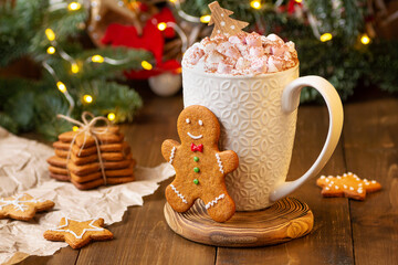 Obraz na płótnie Canvas a mug of hot chocolate with marshmallows stands on a wooden background among Christmas decorations and ginger man cookies. Christmas warming drink, cocoa with cinnamon and marshmallow. new year