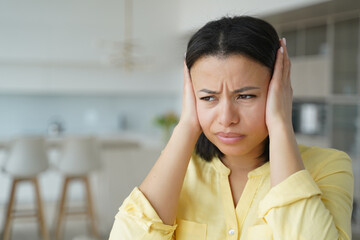 Annoyed nervous female covering ears with hands suffering from loud noise from neighbor's apartment