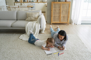 Mother or babysitter and elementary kid daughter paint together lying on floor carpet in living room