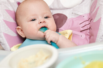 cute baby girl eating with spoon in kitchen