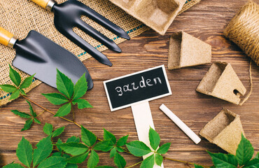 sign for plants on a wooden background with items for sowing: peat pots, herbs, burlap, spatula.