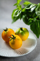 Three yellow tomatoes on a plate with green basil leaves, vertical format