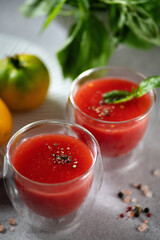 Freshly squeezed tomato juice with basil leaves, salt and pepper in glass glasses on a light gray background, close-up
