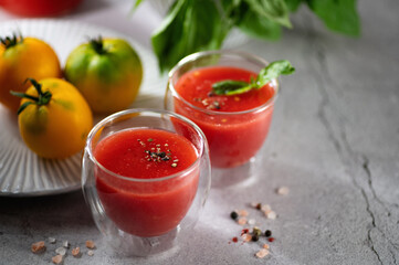 Freshly squeezed tomato juice with basil leaves, salt and pepper in glass glasses on a light gray background, space for text, horizontal format