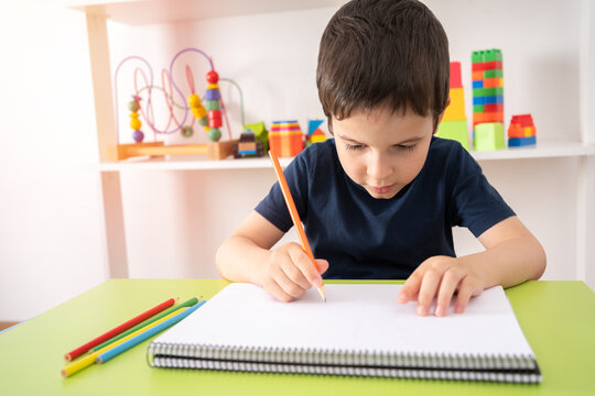 Child hand draws a orange pencil at school