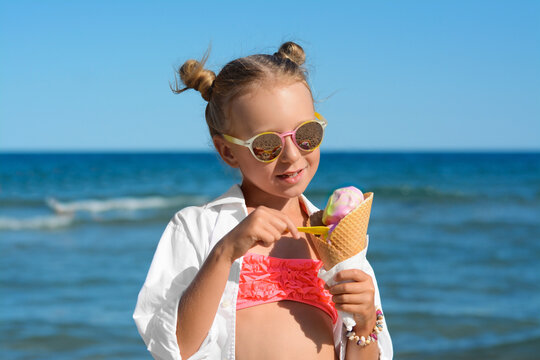 Adorable little girl with delicious ice cream near sea on sunny summer day