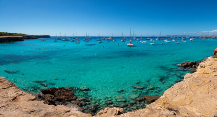 Panoramic view of Cala Saona with sailboats anchored in the Mediterranean Sea
