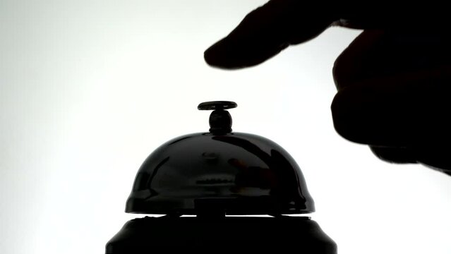 Closeup, isolated, silhouette shot of a hand pressing four times to urgently ring a traditional call / service / reception / concierge bell.