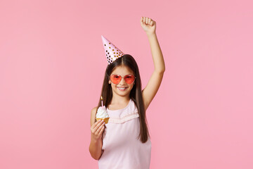 happy little birthday girl with party cone holding cupcake