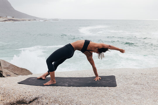 Slim female practicing yoga pose by ocean at coast