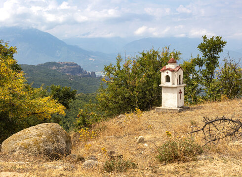 Traditional and memorial roadside small chapel altar or shrine on the side of the road in Greece, Meteora region. The Great Meteoron Holy Monastery of the Transfiguration of the Saviour in background.