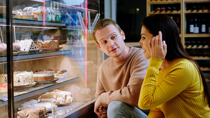 In the cozy bakery cafe happy and excited lady shows to her partner what dessert she wants from the showcase fridge she are very happy
