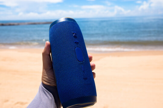 Photo of a man hand holding a portable speaker at the beach 