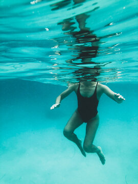 Mature woman's athletic body treading water from underwater perspective in ocean