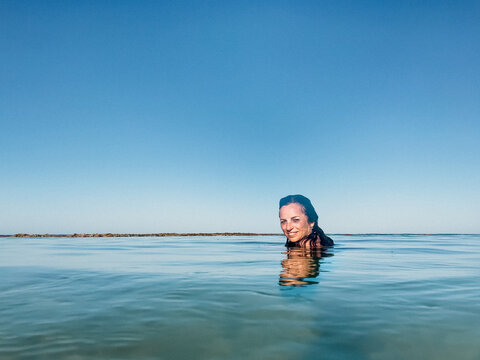 Woman Submerged And Floating In Calm Ocean On Clear Day