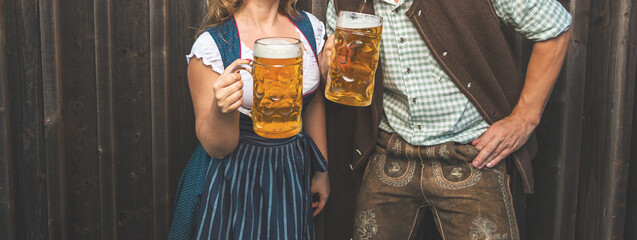 Oktoberfest, woman and man in Bavarian costume with beer mugs - obrazy, fototapety, plakaty