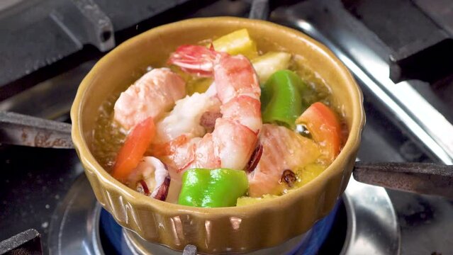 彩り豊かなパプリカやピーマンを添え、グツグツと煮え立つオイルと海老の質感を閉じ込めた「海老のアヒージョ」。ぷりぷりした身の弾力とガーリックの輝きが際立つ一景で、バルの酒肴やパーティの販促に最適な高品質素材です。 | Sizzling shrimp ajillo with colorful bell peppers in boiling garlic oil.
