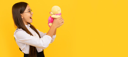 Surprised school age kid hold teddy bear yellow background, toy gift. Banner of child girl with toy, studio portrait, header with copy space.