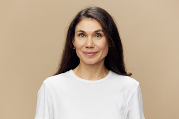 Fototapeta premium a beautiful, surprised woman stands in a white T-shirt on a beige background, holding her hands near her face